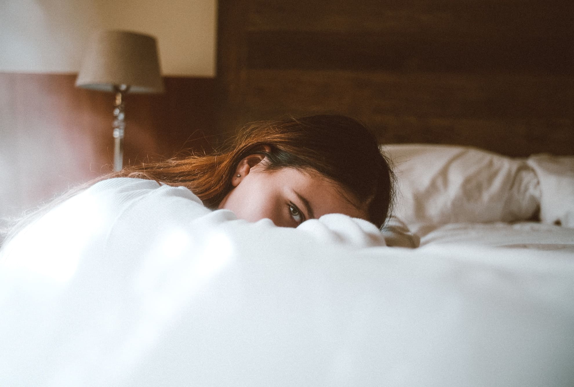 woman lying in bed looking through one eye