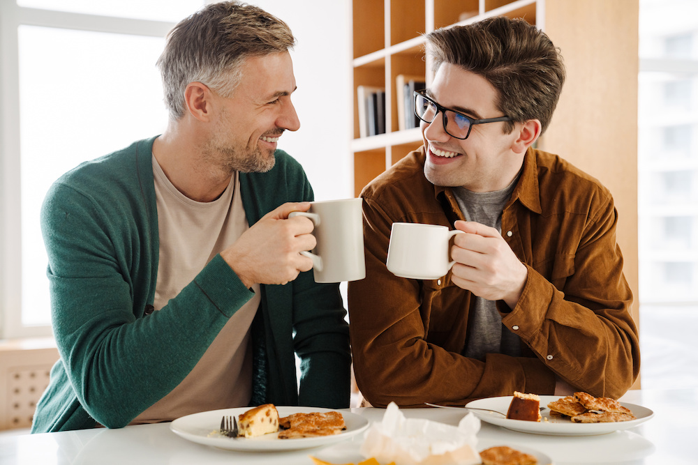 Happy caucasian gay couple drinking coffee while having breakfast