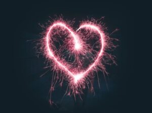 Heart-shaped pink fireworks in black sky.